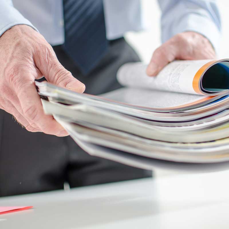 A person wearing ties holds a open book in his hand a a table