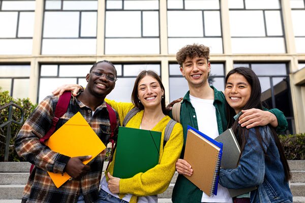 Group of happy and smiling multiracial college students standing in front of university building looking at camera embracing.